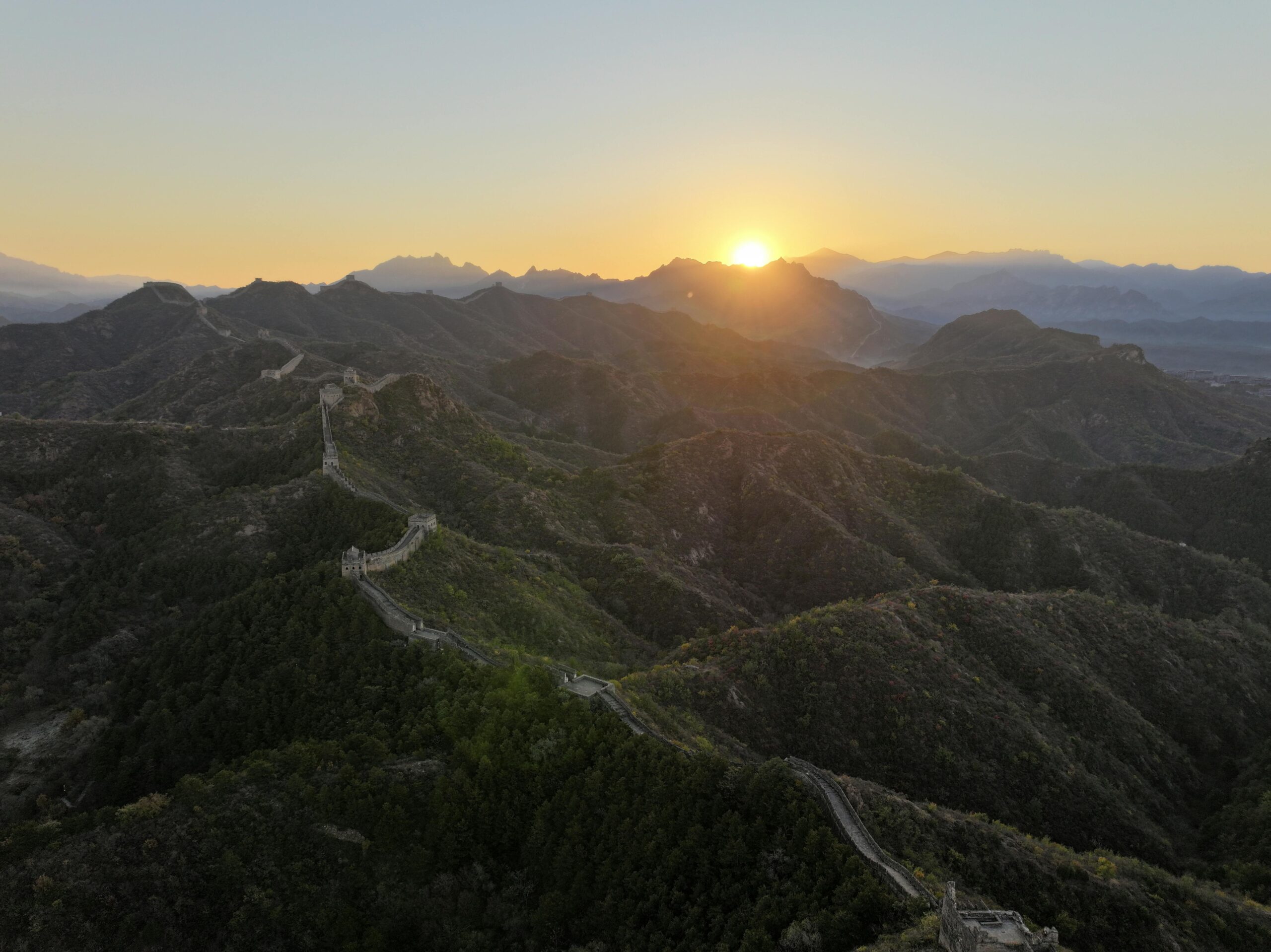 Breathtaking sunrise view of the Great Wall of China winding through lush mountains.